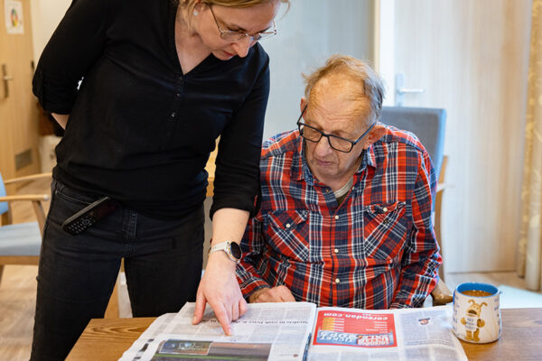 Een bewoner van de Hartekamp Groep leest samen met een begeleider de krant